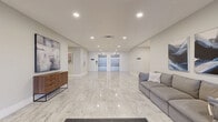The lobby at 49 Brookline Dr in Halifax, Nova Scotia offers a polished and welcoming first impression for residents and visitors alike. Spanning a generously sized single floor, this building entrance is designed with a clean, contemporary aesthetic that balances functionality with refined style.

The space is defined by its striking large-format, marble-look porcelain tile flooring, which reflects the recessed pot lighting above and lends the entire area a bright, open feel. Neutral warm-grey walls keep the atmosphere calm and sophisticated, while curated artwork — including abstract and nautical-themed pieces — adds visual character throughout.

Two seating areas are thoughtfully arranged within the lobby, each furnished with comfortable grey sofas and complementary accent pieces, providing residents with inviting spots to relax or wait. A warm-toned wooden sideboard serves as an elegant focal point near one of the seating zones.

A full-height glass entrance with double doors floods the front of the lobby with natural light and provides easy, accessible entry from the exterior. Two stainless steel elevators are centrally positioned, offering convenient vertical access throughout the building. Additional doors lead to further interior corridors and amenity spaces.

The overall ambiance is modern and professional, creating a clean and comfortable transitional space that sets a welcoming tone for the entire building.