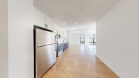 This single-floor, two-bedroom, two-bathroom unit offers a thoughtfully designed layout with a clean, modern aesthetic throughout. Light hardwood-style flooring flows continuously across all rooms, creating a cohesive and bright interior. The open-concept kitchen and living area forms the heart of the unit, with the kitchen featuring a two-tone design: crisp white upper cabinetry paired with dark lower cabinets, white countertops, stainless steel appliances including a refrigerator, range, microwave, and dishwasher, and a matte black faucet. Recessed lighting illuminates the space, which opens into a generously sized living area anchored by large windows with black frames, allowing abundant natural light and outdoor views.

The primary bedroom is a well-proportioned room with access to a walk-in closet equipped with wire shelving for organized storage. The unit includes two full bathrooms, one featuring a glass-enclosed shower with white subway tile, black-framed sliding doors, built-in shelving, and wood-style flooring. A hallway connects the private areas of the unit and includes additional closet space. Throughout, the design emphasizes clean lines, neutral tones, and functional details.