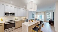 Located at 8005 Gramercy Blvd in Rockville, Maryland, this well-appointed single-floor residence combines modern design with functional living. The open-concept layout seamlessly connects the kitchen, dining, and living areas, creating an inviting and cohesive atmosphere throughout.

The kitchen is a standout feature, outfitted with sleek two-tone cabinetry — high-gloss white uppers paired with warm wood-tone lower cabinets — atop light hardwood-style flooring. A classic white subway tile backsplash, stainless steel appliances, and a generous island with seating complete the space, making it ideal for both cooking and casual dining.

The living room is bright and airy, benefiting from large windows and a sliding glass door that opens to a private balcony, offering abundant natural light and outdoor views. The space features light-toned walls and hardwood-style flooring that carries throughout the main living areas.

The bedroom is tranquil and well-lit, with large windows dressed in sheer curtains and gold-accented hardware, contributing to the residence's cohesive contemporary aesthetic. Neutral tones and carpeted flooring add warmth and comfort.

The bathroom is finished with large-format stone-look tile on both the floors and walls, a wood-tone vanity with a white countertop, and a tub-shower combination, creating a clean and polished look throughout.