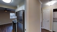 This single-story residence offers a practical and well-appointed layout across two bedrooms and one bathroom. The kitchen is a notable feature, showcasing white cabinetry that extends to the ceiling and is accented with crown molding, lending a clean and timeless aesthetic. Stainless steel appliances, including a full-size refrigerator and a range, provide a modern contrast to the bright cabinetry. A window in the kitchen allows natural light to filter in, enhancing the overall brightness of the space. Dark hardwood-style flooring runs throughout, adding warmth and visual continuity between rooms. Architectural details such as crown molding and clean door casings are present throughout, contributing to a polished, cohesive interior. A hallway connects the main living areas to the bedrooms, which feature closet storage. The neutral wall tones create a versatile backdrop adaptable to a variety of furnishing styles. Overall, the residence balances classic detailing with functional living spaces suited for everyday comfort.