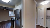 This single-story residence offers a practical and well-appointed layout across two bedrooms and one bathroom. The kitchen is a notable feature, showcasing white cabinetry that extends to the ceiling and is accented with crown molding, lending a clean and timeless aesthetic. Stainless steel appliances, including a full-size refrigerator and a range, provide a modern contrast to the bright cabinetry. A window in the kitchen allows natural light to filter in, enhancing the overall brightness of the space. Dark hardwood-style flooring runs throughout, adding warmth and visual continuity between rooms. Architectural details such as crown molding and clean door casings are present throughout, contributing to a polished, cohesive interior. A hallway connects the main living areas to the bedrooms, which feature closet storage. The neutral wall tones create a versatile backdrop adaptable to a variety of furnishing styles. Overall, the residence balances classic detailing with functional living spaces suited for everyday comfort.