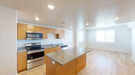This single-floor residence is designed with a clean, modern aesthetic that prioritizes functionality and cohesion. The kitchen serves as a central feature of the space, equipped with warm honey-toned cabinetry, speckled granite countertops, and a full suite of stainless steel appliances including a French door refrigerator with ice maker, electric range, built-in microwave, and dishwasher. A granite-topped kitchen island provides additional workspace and naturally defines the transition into the open-concept living area. Recessed lighting and a textured ceiling add depth to the kitchen and living space, while light-toned hardwood flooring flows continuously throughout, lending warmth and visual consistency.

The living area benefits from natural light through windows fitted with horizontal blinds, creating a bright and airy atmosphere. A bedroom features the same hardwood flooring, a ceiling fan with light fixture, and a window offering natural light and exterior views.

The bathroom is thoughtfully appointed with a wide granite-topped vanity, dual undermount sinks, warm wood cabinetry with brushed nickel hardware, a large mirror, and a tub-shower combination. The overall design of the space is cohesive and contemporary, with neutral tones and quality finishes throughout.