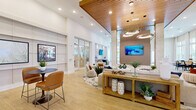 Located at 17800 Sawgrass Bay Blvd in Clermont, Florida, this expansive single-floor clubhouse and amenity space delivers a polished, resort-inspired experience through its contemporary architectural design and high-end finishes. The main lounge area commands attention with soaring ceilings adorned with warm wood slat paneling, complemented by dramatic sculptural pendant lighting and large-format wall-mounted displays. Light wood-toned flooring flows seamlessly throughout, unifying the space with a bright and airy aesthetic. A generously sized social lounge features curated seating arrangements, slatted wood room dividers, and floor-to-ceiling windows that flood the interior with natural light while framing views of the surrounding landscape. A dedicated kitchenette and wet bar area stands out with a bold geometric patterned tile accent wall, white quartz countertops, warm wood cabinetry, and a matte black sink fixture. A glass-enclosed flex room provides a versatile workspace or conference area, benefiting from abundant natural light and a clean, modern interior. Intimate nook seating areas with wainscoted walls and framed nautical artwork offer quieter spaces for conversation or relaxation. Throughout, the design strikes a refined balance between functionality and sophistication, making this a standout community gathering destination.