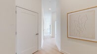 This contemporary single-floor residence is defined by a clean, minimalist aesthetic carried consistently throughout every room. Light hardwood flooring runs seamlessly across the open-concept living and kitchen areas, complementing the crisp white walls and recessed lighting that together create a bright, airy atmosphere. The living area benefits from expansive floor-to-ceiling windows with black frames, inviting abundant natural light and offering open views of the surrounding urban streetscape. The kitchen is designed for both function and style, featuring high-gloss white cabinetry extending to the ceiling, a white quartz peninsula with bar seating, subway tile backsplash, and a full suite of stainless steel appliances. A connecting hallway, accented with framed artwork, leads to the private quarters. The bedrooms are generously proportioned with tall ceilings and light-toned flooring, providing a calm and restful environment. The bathrooms maintain the home's modern sensibility, finished with large-format neutral tiles, a glass-enclosed walk-in shower, and clean white vanities. Throughout, the design prioritizes natural light, open sightlines, and a refined, contemporary palette that gives the entire residence a cohesive and polished character.