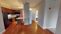 Located in the heart of Chicago's Loop neighborhood at 149–167 N Wabash Ave, this single-floor unit offers a well-designed open layout with a cohesive blend of functional and modern finishes throughout. Rich hardwood flooring—characterized by a distinctive striped grain pattern—extends across the main living areas, reflecting light and adding warmth to the space.

The kitchen is a standout feature, outfitted with rich cherry wood cabinetry that extends to the ceiling, offering substantial storage. A mosaic tile backsplash, granite-style countertops, a stainless steel sink, and black appliances—including a refrigerator, dishwasher, and range—complete the kitchen's practical yet polished design. A peninsula with bar-height seating provides an informal dining option and visually anchors the kitchen's connection to the open living area.

The living space is generous and open, with soaring ceilings that amplify the sense of volume. A pair of large windows frames views of Chicago's urban skyline, filling the room with natural light. Track lighting throughout provides adjustable, focused illumination.

The bathroom is clean and bright, finished with white floor tiles and white subway-tiled walls surrounding a full soaking tub and shower combination, complemented by a dark wood vanity.