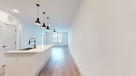 This single-floor residence offers a clean, modern aesthetic with light wood-tone flooring and crisp white walls throughout the main living areas. The open-concept layout seamlessly connects the kitchen and living room, creating a bright and airy atmosphere enhanced by natural light from a front-facing window. A ceiling fan anchors the living area, which also features a glass-paneled entry door that further invites natural light inside.

The kitchen is a standout feature, boasting white shaker cabinetry with matte black hardware, a herringbone tile backsplash, and a full suite of stainless steel appliances including a French door refrigerator, range, microwave, and dishwasher. A peninsula with a white countertop and an undermount sink is topped by stylish black pendant lights, providing both functionality and a modern design focal point. A built-in mudroom nook with hooks and shelving sits conveniently adjacent to the kitchen.

The bedroom offers plush carpet flooring, dual windows with blinds, a ceiling fan, and generous natural light. The bathroom features light wood-tone flooring, a marble-tiled walk-in shower with black fixtures, a glass door, and a white vanity. The dedicated laundry room includes a stacked washer and dryer unit alongside extensive built-in shelving and closet organization, maximizing storage efficiency throughout the home.