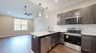 Located at 1550 Empire Blvd in Webster, NY, this thoughtfully designed 2-bedroom, 1-bathroom residence offers a clean, contemporary aesthetic across a single floor. The open-concept kitchen, dining, and living area serves as the heart of the home, anchored by a peninsula with a white quartz countertop and bold navy cabinetry. Dark shaker-style cabinetry lines the kitchen walls, complemented by a white tile backsplash and a full suite of stainless steel appliances, including a refrigerator, electric range, microwave, and dishwasher. Warm hardwood-style flooring flows throughout the main living areas, adding continuity and depth. Vaulted ceilings with recessed lighting and pendant fixtures lend an airy, elevated feel to the main living space, which also features a ceiling fan and a window that invites natural light. The primary bedroom is a comfortable retreat with vaulted ceilings, a window with a serene outdoor view, and recessed lighting. The bathroom is finished with marble-style tile flooring, a dark vanity with white countertop, and a glass-enclosed walk-in shower. Three closets and a dedicated laundry area provide generous storage and convenience throughout this well-appointed home.