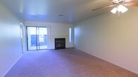 This single-floor space offers a clean and functional layout designed for comfortable living. The main living area is finished with wall-to-wall carpeting that adds warmth underfoot, while neutral-toned walls create a bright, versatile backdrop suitable for a variety of décor styles. A standout feature of the living area is the classic fireplace, framed by a simple mantel and set against the wall, providing a natural focal point and a cozy gathering spot. Adjacent to the fireplace, a narrow vertical accent window draws in an additional sliver of natural light, complementing the generous illumination provided by the large sliding glass door. The sliding door opens to an outdoor area, seamlessly connecting the interior to the exterior and allowing abundant daylight to fill the room. Ceiling-mounted HVAC vents are integrated throughout, ensuring year-round climate comfort. The overall ambiance of the space is clean, open, and move-in ready, with a straightforward design that prioritizes functionality and livability. The single-floor layout offers ease of accessibility throughout the home.