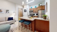 This single-floor residential unit at 1401 Forensic Science Dr in Huntington, West Virginia, is designed to accommodate student living with a practical and modern aesthetic. The open-concept kitchen serves as a central hub, featuring warm-toned wood cabinetry, granite countertops, and a full suite of stainless steel appliances including a range, microwave, and refrigerator. A large kitchen island with an integrated sink and bar seating provides additional workspace and a casual dining option, while light wood-look flooring ties the kitchen seamlessly into the adjacent living area.

Multiple bedrooms offer comfortable, functional spaces, each carpeted and sized to accommodate a bed and dedicated study desk. Select rooms include natural light from windows with blinds and curtains, while built-in or freestanding storage units provide organizational flexibility. The neutral color palette throughout the bedrooms creates a calm, focused environment suited to academic life.

The bathroom is finished with rich wood cabinetry, granite countertops, a dual-sink vanity with brushed nickel hardware, and a large wall mirror with overhead lighting. Light tile flooring completes the clean, contemporary look. Overall, the unit balances functional design with comfortable, modern finishes throughout.