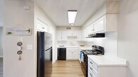 This single-floor, 2-bedroom, 1-bathroom home offers a functional and clean layout with consistent design throughout. Light-toned laminate hardwood flooring runs across the main living areas and bedrooms, complemented by neutral-toned walls and white baseboards that give the space a bright, cohesive feel. The living room is an open, generously sized area with a textured ceiling, providing a welcoming gathering space. It flows naturally into the combined dining room and kitchen, where crisp white cabinetry lines the walls from floor to ceiling, offering ample storage. The kitchen is equipped with black appliances including a refrigerator, dishwasher, and electric range, paired with light stone countertops and a skylight fixture that enhances illumination. A dedicated pantry provides additional storage convenience. Both bedrooms are comfortably sized, each featuring ceiling fans, large windows that allow natural light to fill the rooms, and access to closets. The primary bedroom is notably spacious, with its own ceiling fan and a window offering outdoor views. The bathroom includes a white vanity with a single sink, a large mirror with overhead lighting, and a bathtub. A hallway connects the main living areas to the private bedroom and bathroom wing, with a total of three closets distributed throughout the home for generous storage capacity.