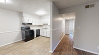 Located at 320 Spruce St in Spartanburg, SC, this single-story home offers four bedrooms and two bathrooms within a practical and efficient layout. The combined kitchen and living area serves as the heart of the home, featuring light wood-look flooring, white cabinetry, a black electric range, a built-in dishwasher, and a black refrigerator. A half-wall partition separates the kitchen from the adjoining living space, which receives natural light through a large sliding window with blinds. The neutral gray walls and textured ceilings carry throughout the home, creating a consistent and clean aesthetic. The four bedrooms are carpeted for comfort, each offering closet space — including one bedroom with a generous walk-in closet and a large window overlooking greenery. The primary bedroom provides a comfortable footprint with its own closet. Two hallways connect the bedrooms and living areas, supporting smooth circulation throughout the home. The two bathrooms include one with a pedestal sink and mirror with vanity lighting, and another with a warm wood-toned vanity, stone-look countertop, and wood-look tile flooring. This home offers a straightforward, functional design well-suited for everyday living.