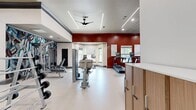 This 1,330-square-foot fitness center at 50 Estuary Trail in Alpharetta, Georgia, is a single-floor facility designed to support a comprehensive workout experience. The space is divided into distinct training zones, each thoughtfully outfitted with a wide selection of equipment. The cardio area features treadmills and elliptical machines positioned along a bold, deep-red accent wall adorned with gold-framed mirrors, creating a dynamic and energizing atmosphere. The strength training zone is equipped with multiple cable machines, multi-function weight stations, a dumbbell rack, and free weight equipment from brands including Life Fitness. A dedicated open-floor area provides ample room for functional training, complemented by plyo boxes and additional cable systems. The facility's interior design is polished and modern, with white walls, dark crown molding, recessed LED lighting, linear light fixtures, and ceiling fans throughout to ensure comfort during workouts. A vibrant geometric-patterned accent wall adds a striking visual focal point to the open training floor. The durable, light-toned fitness flooring spans the entire space, offering both safety and ease of maintenance. The layout is open and spacious, allowing for easy movement between equipment zones while maintaining a clean, professional aesthetic.