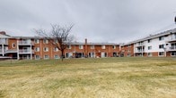 This single-floor residence offers a straightforward and functional layout designed for comfortable everyday living. The unit features one bedroom and one bathroom, providing an efficient use of space well-suited for individuals or couples. The building itself is constructed of classic red brick, lending a timeless and durable character to the exterior. The structure is part of a multi-unit complex, and the exterior view reveals a generous shared green space at the rear of the building — a sizable open lawn area that adds a sense of openness and provides outdoor space for residents. The building's design is traditional, with evenly spaced windows that allow natural light to enter the units. The rear of the building also features individual patio or entry access points for ground-level units. The overall setting presents a quiet, residential atmosphere with mature trees nearby. While interior image details were limited, the unit's single-floor configuration ensures easy accessibility and a cohesive living environment. The combination of a classic brick exterior, shared green surroundings, and a practical one-bedroom floor plan makes this a functional and straightforward residential space.