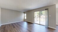 Located at 2322 Spring House Ln in Augusta, GA, this single-story unit offers three bedrooms, two bathrooms, a dedicated dining room, and a combined kitchen and living area within a efficiently arranged floor plan. Neutral-toned walls and white baseboards create a clean, cohesive aesthetic throughout.

The living room is one of the more prominent spaces, featuring dark wood-style laminate flooring, a textured ceiling, and a sliding glass door that opens to a private balcony with outdoor views of surrounding trees, allowing natural light to fill the room. A secondary window further brightens the space.

The kitchen is equipped with gray cabinetry, light stone-pattern countertops, and black appliances including a range and refrigerator, all set over matching wood-style flooring. The dining area is situated adjacent to the kitchen for convenient flow.

The bedrooms offer a mix of finishes — some feature carpet flooring while others continue the wood-style laminate — all with neutral walls and ample wall space. The primary bedroom provides a comfortable, well-proportioned retreat.

The two bathrooms include a vanity with gray cabinetry and a stone-pattern countertop paired with a large mirror, as well as a tub-shower combo with white tile surround, wood-style flooring, and accessible grab bars.