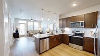 Located at 1450 Valley Ridge Blvd in Lewisville, TX, this 2-bedroom, 1-bathroom residence offers a thoughtfully designed single-floor layout with modern finishes and a bright, welcoming ambiance. The open-concept kitchen and living area serves as the heart of the home, where rich dark-walnut cabinetry, granite countertops, a subway tile backsplash, and a full suite of stainless steel appliances make the kitchen both functional and visually striking. Pendant lighting over the breakfast bar adds warmth, while light hardwood-style flooring flows seamlessly throughout the main living areas. The living room benefits from large windows fitted with horizontal blinds, flooding the space with natural light and providing views of the surrounding community. A glass-panel door leads to an outdoor area, further enhancing the airy feel. Both bedrooms feature plush carpeting, ceiling fans, and generously sized windows. The primary bedroom includes a walk-in closet with built-in shelving, offering practical storage. The bathroom is finished with hardwood-style flooring, a granite-topped vanity with dark cabinetry, and a glass-enclosed walk-in shower with white tile surround. A hallway connects all rooms efficiently, completing this cohesive and comfortable living space.