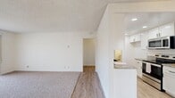 Located at 23920 Anza Ave in Torrance, CA, this single-story 2-bedroom, 1-bathroom unit offers a well-organized layout with a clean, neutral aesthetic throughout. The living room is generously sized, featuring plush carpeting, a textured ceiling, and a wide sliding glass door with vertical blinds that fills the space with natural light and provides access to an outdoor patio area. Adjacent to the living room is a fully renovated kitchen equipped with white shaker cabinetry, granite countertops, a mosaic tile backsplash, a black undermount sink, recessed lighting, and stainless steel appliances including a range, microwave, and dishwasher. Wood-look vinyl flooring runs through the kitchen and hallway, while soft carpet extends into all living and sleeping areas. Both bedrooms are well-proportioned with natural light from windows; the primary bedroom is notably spacious and includes a large walk-in closet with built-in shelving rods on multiple walls. The bathroom features a white vanity with granite countertop, wood-look flooring, and modern black hardware accents. A hallway connects all rooms efficiently, completing this thoughtfully designed, move-in-ready unit in a desirable South Bay neighborhood.