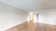Located at 3454 Ruffin Rd in San Diego, CA, this one-bedroom, one-bathroom residence offers a well-organized layout across a single floor. The living room is bright and open, featuring warm wood-style plank flooring, crisp white walls, and a textured ceiling. A sliding glass door with vertical blinds fills the space with natural light and provides outdoor views, while a ceiling fan adds comfort to the room. The combined kitchen and living area is thoughtfully designed, with the kitchen showcasing white cabinetry, a stainless steel sink, and black appliances including a refrigerator and dishwasher. A skylight-style ceiling fixture brightens the kitchen, which also features a window for additional natural light. The spacious primary bedroom offers generous closet space with full-width sliding panel doors, wood-style flooring, and a large window that invites natural light. The bathroom is clean and functional, featuring a full tub-shower combination with white tile surround, wood-toned hardware accents, and matching flooring. A hallway connects the rooms efficiently, contributing to the cohesive and practical flow of the residence. The overall aesthetic is clean, neutral, and move-in ready.