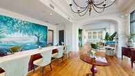 Located at 101 Cay Plaza in Savannah, Georgia, this sophisticated single-floor clubhouse spans a generously sized footprint designed to accommodate both social gatherings and quiet retreats. The space seamlessly blends classic Southern architectural details with contemporary touches throughout its multiple living and dining areas.

The reception and dining lounge area is anchored by warm hardwood flooring, elegant crown molding, and a striking large-scale landscape painting that pays homage to Savannah's iconic scenery. A long marble-topped counter with richly stained wood cabinetry serves as the central feature, complemented by mint-green upholstered chairs and a decorative chandelier overhead.

One living area showcases soaring ceilings with floor-to-ceiling arched windows that flood the space with natural light and offer sweeping outdoor views. Rich leather wingback chairs, a grand piano tucked behind steel-framed glass partitions, and lush tropical plants contribute to an inviting, sophisticated atmosphere. An adjacent lounge features sage-green velvet seating, detailed wainscoting, wall sconces, and arched windows that reinforce the space's refined character.

A second living area presents a more modern aesthetic, with large-format tile flooring, dramatic double-height windows, cognac leather armchairs arranged around a central fireplace, and an eye-catching sculptural pendant light fixture. A well-organized mail center with exposed brick walls rounds out the amenities, offering both function and charm.