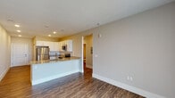 This single-floor residence in Colorado Springs, Colorado, offers a well-designed open-concept layout finished with consistent, modern materials throughout. Dark hardwood-style flooring flows through the main living and kitchen areas, creating a cohesive and polished aesthetic against neutral warm-gray walls and crisp white baseboards.

The kitchen is a functional centerpiece of the space, outfitted with white shaker-style cabinetry, granite countertops, and a full suite of stainless steel appliances, including a refrigerator, range, and over-the-range microwave. A peninsula with a built-in sink extends into the living area, providing additional prep space and a natural division between the kitchen and the open living room.

The living area is generously proportioned, with recessed lighting and access to an outdoor balcony through a sliding glass door dressed with vertical blinds, offering views of the surrounding Colorado landscape. A bedroom features plush carpeting, a ceiling fan, and a window that frames scenic outdoor views, while another room continues the hardwood-style flooring theme. The bathroom includes a soaking tub with full tile surround in a warm stone finish, wood-style flooring, and chrome fixtures, combining practicality with a refined finish.
