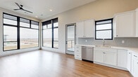 This thoughtfully designed 2-bedroom, 2-bathroom unit in Ankeny, Iowa offers a modern, open-concept layout with a clean, contemporary aesthetic throughout. The combined kitchen and living area serves as the heart of the home, featuring warm wood-look flooring, soaring ceilings, and dramatic floor-to-ceiling windows with bold black frames that flood the space with natural light and frame sweeping outdoor views of the surrounding landscape. The kitchen is well-appointed with white shaker cabinetry, light countertops, a classic subway tile backsplash, and a full suite of stainless steel appliances, including a range, microwave, dishwasher, and refrigerator. A private balcony is accessible directly from the living area. Both bedrooms are generously proportioned, continuing the wood-look flooring and neutral palette, with the primary bedroom offering a spacious walk-in closet and a private ensuite bathroom. The bathrooms are finished with white cabinetry, illuminated mirrors, and clean modern fixtures. Hallways are bright and well-organized, with additional closets providing ample storage. An in-unit laundry area adds everyday convenience. The unit's design prioritizes natural light, open sightlines, and functional storage throughout.