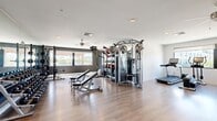 Located at 947 Myers St in Richmond, Virginia, this fitness center offers a well-appointed, single-floor workout facility designed to support a full range of exercise routines. The space features durable wood-look flooring throughout, white walls accented by dark gray lower panels, and a clean, modern aesthetic that creates an energizing atmosphere.

The cardio zone is equipped with multiple treadmills, cycling bikes, an elliptical, a stair climber, and a rowing machine, all positioned in front of wall-mounted flat-screen televisions. Ceiling fans provide additional air circulation throughout the space. Natural light flows in through several windows along the walls, offering views of the surrounding outdoor area.

The strength training section is equally comprehensive, featuring a large multi-function cable machine, a Hammer Strength power rack loaded with weight plates, a full dumbbell rack, adjustable weight benches, TRX suspension trainers, and a selection of medicine balls. Floor-to-ceiling mirrors along one wall enhance the sense of openness and allow users to monitor their form during workouts.

The entrance area provides open floor space ideal for stretching or functional training, and easy-clean flooring makes maintenance straightforward. Overall, this fitness center is thoughtfully organized to accommodate a wide variety of training styles in a bright, functional, and motivating environment.