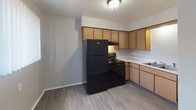 This single-floor unit offers a straightforward, functional layout with clearly defined living spaces. The kitchen is equipped with light wood cabinetry providing generous storage, a black refrigerator and electric range, a built-in sink, and light-toned countertops. Wood-look luxury vinyl flooring runs throughout the kitchen and extends into the main living areas, lending a cohesive and easy-to-maintain aesthetic.

The living area is open and neutrally finished with light gray walls, wood-look flooring, and a textured ceiling. A window unit air conditioner and baseboard heating system provide climate control year-round. Natural light filters in through windows dressed with vertical blinds, offering views of the surrounding greenery.

The bedroom features plush gray carpeting, a textured ceiling, baseboard heating, and a window with vertical blinds that allows natural light. A closet opening is visible from the adjoining living space.

The bathroom is cleanly appointed with a white tiled tub-and-shower combo, a toilet, and a vanity with a wood-toned cabinet base. Stainless steel grab bars are installed at the tub and shower area, providing added accessibility and safety. Wood-look flooring completes the bathroom's clean, utilitarian finish.