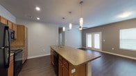 Located at 216 Claggett St in San Antonio, TX, this single-story residence offers a well-designed open-concept layout that promotes a seamless flow between the kitchen and living areas. The kitchen serves as a central hub, anchoring the space with a generously sized island topped with granite-style countertops and an integrated double sink. Warm-toned wood cabinetry provides ample storage, complemented by a mosaic tile backsplash, black appliances including a refrigerator, electric range, microwave, and dishwasher, and recessed lighting alongside stylish cylindrical pendant lights that hang above the island.

The living area extends naturally from the kitchen, featuring dark hardwood-style flooring, neutral gray walls, and a ceiling fan that enhances comfort. French doors open to the exterior, allowing natural light to fill the space. A separate bedroom offers plush carpeting, two windows with blinds, and a ceiling fan, creating a quiet and comfortable retreat. The bathroom includes a full soaking tub with white tile surround. Throughout the home, consistent finishes and a neutral color palette contribute to a cohesive and inviting overall ambiance.