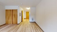 Located at 1240 SW Columbia St in Portland, Oregon, this efficiently designed studio unit makes thoughtful use of its single-floor layout. The open-concept main area seamlessly combines the living, dining, and kitchen functions into one cohesive space. Light-toned hardwood-style flooring runs throughout, lending a clean, modern feel and visually expanding the area. Natural light filters in through wood-trimmed windows, brightening the neutral cream-colored walls and creating a welcoming ambiance.

The kitchen is equipped with warm maple-toned cabinetry and includes a full-size refrigerator, providing practical functionality within a compact footprint. A track lighting system in the main living area offers flexible, adjustable illumination. An electrical panel is conveniently built into the wall near the entryway, alongside a wall-mounted heater unit.

The full bathroom features tile flooring in soft, warm tones, a soaking tub, toilet, and a vanity with matching maple cabinetry, maintaining the consistent warm-wood design language found throughout the unit. A dedicated closet with double wood-panel doors provides essential storage. Textured ceilings are present throughout the space, adding a subtle architectural detail. The unit's practical layout and consistent finishes make it a functional and tidy living space in the heart of Portland.