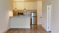 Located at 408 Northampton Rd in Amherst, Massachusetts, this single-floor unit showcases a clean, modern design with consistent wood-look flooring flowing throughout every room. The open-concept kitchen serves as a central highlight, featuring gray shaker-style cabinetry, a herringbone tile backsplash, granite countertops, and stainless steel appliances including a refrigerator and microwave. A peninsula with a granite surface and pendant lighting overhead adds both function and style, making it ideal for casual dining or entertaining. The unit includes generously sized bedrooms with soaring ceilings that enhance the sense of openness. One bedroom features a built-in closet with bifold doors, while another benefits from natural light streaming through a window with outdoor views of surrounding greenery. Two full bathrooms are finished with granite-topped vanities, gray cabinetry, wood-look flooring, and tub-shower combinations with curved curtain rods. The living areas are bright and airy, with tall ceilings and neutral white walls that complement the warm tones of the flooring. The overall ambiance is fresh, contemporary, and move-in ready, offering a well-appointed living experience in a convenient Amherst location.