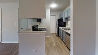 This single-floor unit offers a practical and comfortable layout with thoughtful finishes throughout. The main living area welcomes residents with warm hardwood-style flooring, neutral gray walls, and a ceiling fan with a light fixture, creating a bright and airy atmosphere. A sliding glass door with vertical blinds allows natural light to flow in while providing access to an outdoor view. A secondary living or dining area shares the same flooring and features a ceiling fan, maintaining a consistent aesthetic throughout the common spaces. The kitchen is efficiently designed with gray shaker-style cabinetry, light granite-style countertops, a subway tile backsplash, and black appliances including a range and refrigerator, complemented by a stainless steel dishwasher and sink. The bedrooms feature plush carpeting, large windows with horizontal blinds that invite natural light, and sliding closet doors for convenient storage. The bathroom is well-appointed with a tub and shower combo featuring white tile surround, a gray vanity with granite-style countertop, a single sink, and a lighted mirror. The textured ceilings and clean white trim work are consistent throughout, contributing to the unit's cohesive and move-in ready presentation.