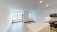 Located in Dayton, KY, this thoughtfully designed single-floor residence offers a clean, modern aesthetic throughout. The open-concept layout seamlessly connects the kitchen and living area, creating a bright and airy atmosphere. Large windows in the living space flood the interior with natural light and frame views of lush greenery, complemented by a ceiling fan for added comfort.

The kitchen is a standout feature, outfitted with white shaker-style cabinetry, a subway tile backsplash, a central island with a white countertop, and a full suite of stainless steel appliances including a refrigerator, range, microwave, and dishwasher. Light hardwood-style flooring runs consistently throughout the entire unit, reinforcing the cohesive, contemporary feel.

The bedroom is a serene retreat, featuring a ceiling fan, a horizontal clerestory window that allows natural light while maintaining privacy, and a spacious closet. The full bathroom includes a white vanity with a wide mirror and a combined tub and shower unit. A separate half bathroom provides additional convenience, complete with a white vanity, cabinet storage, and a mirror. Recessed lighting and crisp white walls round out the clean, modern design of this well-appointed Dayton residence.