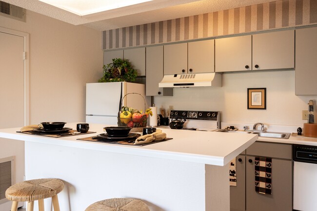 A spacious kitchen with hanging cabinets, a stove, and open counter space creates a homely cooking environment. - The Lakes Apartments