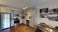 Located at 603 Rigsbee Ave in the heart of Durham, NC, this single-floor residence offers a well-designed, contemporary living environment with thoughtful finishes throughout. The open-concept layout connects the living, dining, and kitchen areas seamlessly, creating a cohesive and functional space ideal for everyday living and entertaining.

The kitchen is appointed with stainless steel appliances, including a range, microwave, dishwasher, and refrigerator. Light wood-toned cabinetry extends to the ceiling, providing generous storage, while granite countertops and a classic tile backsplash contribute a polished, modern aesthetic. Rich hardwood-style flooring runs throughout the main living area, adding warmth and continuity.

The living area is spacious and bright, benefiting from a ceiling fan and access to a private balcony through glass French doors, allowing natural light to flow in and offering outdoor views. The dining area comfortably accommodates a round table and chairs, situated conveniently adjacent to the kitchen.

The bedrooms feature plush carpeting, ceiling fans, and ample closet space, including a walk-in closet in the primary bedroom. The bathroom includes a glass-enclosed walk-in shower with tile surround, complemented by neutral tile flooring and modern cabinetry with granite countertops. Overall, the unit presents a clean, contemporary ambiance throughout.