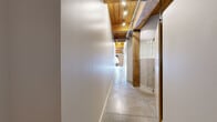 This industrial-style loft masterfully combines historic architectural character with modern finishes across a single, well-organized floor. The open-concept living, dining, and kitchen area serves as the heart of the space, showcasing soaring wood-planked ceilings supported by heavy timber beams and structural columns. Exposed ductwork adds an authentic industrial aesthetic, while polished concrete floors reflect natural light streaming through dramatic arched brick windows along the exterior wall. The kitchen features warm wood cabinetry, granite countertops with a generous breakfast bar, black appliances, and track lighting overhead. A long hallway connects the main living area to the private quarters, flanked by richly textured wood columns and accessing the three bathrooms, one of which includes a curved glass block shower enclosure alongside a soaking tub. The spacious primary bedroom continues the loft's industrial aesthetic with concrete floors and exposed timber ceiling details. A dedicated utility room and closet provide practical storage solutions. Throughout the space, the interplay of exposed brick, natural wood, polished concrete, and abundant sunlight creates a warm yet distinctly urban ambiance.