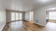 This single-story, 2-bedroom, 1-bathroom home offers a practical and comfortable layout across a thoughtfully organized floor plan. The living room is a standout space, featuring warm wood-look flooring, neutral gray walls, a textured ceiling, and a set of French doors that flood the room with natural light and provide outdoor access. A hallway connects the main living areas to the private quarters of the home.

The galley-style kitchen is efficiently designed with dark cabinetry lining both sides, light countertops, a double-basin sink, and a full suite of black appliances including a range, microwave, refrigerator, and dishwasher. A window at the end of the kitchen provides additional natural light.

The two bedrooms are carpeted in a neutral beige tone, offering a soft and quiet retreat. The primary bedroom is a comfortable size and is accompanied by a dedicated walk-in closet outfitted with dual wire shelving and hanging rods. The second bedroom is equally functional with ample wall space and multiple electrical outlets.

The single full bathroom features wood-look tile flooring, a dark vanity with a speckled countertop, a large mirror, and a tiled shower-tub combination. The space is finished with clean, neutral tones throughout, creating a cohesive and move-in ready environment.