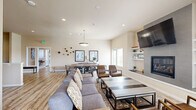 Located in Airway Heights, Washington, this single-floor community amenity space offers a thoughtfully designed layout that caters to a variety of social and recreational needs. The open-concept kitchen, dining, and living area serves as the heart of the space, featuring a bright, modern kitchen outfitted with white shaker cabinetry, stainless steel appliances, track lighting, and light hardwood-style flooring that extends throughout. The adjacent dining area is bathed in natural light from large windows and is anchored by a rustic wood dining table beneath a statement pendant light, complemented by contemporary wall art and decorative accents. The main living room is a standout, showcasing a tile-surround fireplace flanked by built-in shelving and a wall-mounted television, creating a warm and inviting focal point. A dedicated cinema lounge provides a more intimate entertainment setting, complete with plush leather recliners, a sectional sofa, surround sound speakers, and cinema-themed décor. The spacious fitness center rounds out the amenities, boasting vaulted ceilings, abundant natural light, durable rubberized flooring, treadmills, ellipticals, a cable machine, free weights, and wall-mounted televisions — offering a comprehensive workout environment within the community.