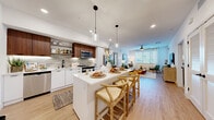 Located at 1542 Bartlett Ln in Sacramento, CA, this well-designed single-story home offers 2 bedrooms and 2 bathrooms across a thoughtfully laid-out floor plan. The open-concept kitchen and living area serves as the heart of the home, featuring white lower cabinetry paired with warm walnut upper cabinets, a textured tile backsplash, stainless steel appliances, and a large kitchen island with a white quartz countertop illuminated by pendant lighting. Light wood-tone flooring flows throughout the main living areas, enhancing the bright and airy atmosphere. The living room receives ample natural light through large windows dressed with horizontal blinds. Both bedrooms are comfortably sized, with plush carpeting, ceiling fans, and windows that invite natural light. The primary suite includes a spacious walk-in closet with built-in shelving and direct access to a well-appointed en-suite bathroom featuring a walnut vanity, white quartz countertop, backlit mirror, and a glass-enclosed shower. The second bathroom mirrors the same refined aesthetic. A dedicated laundry area and two closets add practical functionality. The overall design is clean and contemporary, with a neutral color palette and modern fixtures throughout.