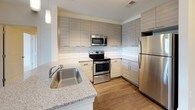 This single-floor, 2-bedroom, 2-bathroom residence combines modern design with functional living spaces throughout. The entryway opens to a well-lit foyer with dark hardwood-style flooring, multiple closets for ample storage, and clean white panel doors that carry consistently through the unit.

The living area features the same rich hardwood-style flooring and neutral walls, with a sliding glass door leading to a private balcony offering outdoor views of surrounding greenery. The kitchen is outfitted with contemporary flat-panel cabinetry in a light gray wood-grain finish, a white subway tile backsplash, granite countertops, stainless steel appliances including a refrigerator, range, and microwave, and a single-basin undermount sink.

Both bedrooms are carpeted in a light neutral tone and receive generous natural light through large windows. One bedroom includes a ceiling fan. The two bathrooms each reflect a clean, modern aesthetic. One features a granite-topped vanity, large-format white tile flooring, and a soaking tub, while the other offers a walk-in glass-enclosed shower with floor-to-ceiling white tile and brushed chrome fixtures. Together, the spaces present a cohesive, well-finished interior.