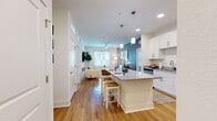 Located at 900 SE Third Ave in Ocala, FL, this 2-bedroom, 2-bathroom residence offers a thoughtfully designed single-floor layout that balances comfort and modern style. The open-concept living and kitchen area serves as the heart of the home, where warm hardwood-style flooring flows seamlessly throughout. The kitchen is well-equipped with crisp white shaker cabinetry, granite countertops, stainless steel appliances including a refrigerator, range, and microwave, and a central island with pendant lighting that doubles as a casual dining space. The living room features a ceiling fan, large windows that invite natural light, and a neutral color palette with a tasteful accent wall. The spacious primary bedroom features plush carpeting, a large window with outdoor views, and direct access to a dedicated closet. Both bathrooms are finished with granite-topped vanities, white cabinetry, and hardwood-style flooring — one featuring a tub-shower combination and the other a walk-in shower configuration. A second bedroom and additional closet provide versatile storage and living options. Clean white walls, recessed lighting, and consistent finishes throughout create a cohesive, modern ambiance across the entire residence.