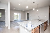 This single-floor residence is designed with an open, flowing layout that connects the kitchen and living areas seamlessly. The kitchen serves as a central hub, featuring warm-toned wood cabinetry extending to the ceiling, granite countertops, and a large island with an undermount sink and pendant lighting overhead. Stainless steel appliances, including a range, refrigerator, and microwave, complete the well-appointed cooking space. Wood-style flooring runs throughout the kitchen and living area, transitioning to plush carpeting in the living room, which opens to a private balcony through a sliding glass door, inviting natural light and outdoor views.

The bedrooms are generously sized, each carpeted and equipped with ceiling fans and windows overlooking lush green surroundings. The bathrooms are finished with granite-topped wood vanities, large mirrors, and tub-shower combinations with brushed nickel fixtures and grab bars. Neutral gray walls throughout the unit create a cohesive, calm aesthetic, while recessed lighting and modern pendant fixtures provide consistent illumination across all spaces. The overall ambiance is clean, contemporary, and functional.