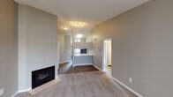 This single-floor residence offers a practical and comfortable layout with a cohesive neutral color palette of warm grays and beige tones throughout. The living area is a standout space, featuring vaulted ceilings that enhance the sense of openness, plush carpeting, a tile-surround fireplace, and a sliding glass door with vertical blinds that invites natural light. The space flows directly into a dining area and an open kitchen, which is defined by a breakfast bar countertop, dark espresso cabinetry reaching toward the ceiling, light granite-style countertops, and a full suite of stainless steel appliances including a range, built-in microwave, and dishwasher. The kitchen is finished with light tile flooring, contrasting with the wood-look flooring found in the transitional areas. The bedrooms are carpeted and well-sized, each offering closet storage — one featuring a sliding-door closet with built-in shelving and hanging rod. Two full bathrooms serve the residence, each equipped with a tub-shower combination, stone-topped dark vanity, and wood-look flooring, providing a consistent and clean aesthetic throughout the home.