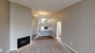 This single-floor residence offers a practical and comfortable layout with a cohesive neutral color palette of warm grays and beige tones throughout. The living area is a standout space, featuring vaulted ceilings that enhance the sense of openness, plush carpeting, a tile-surround fireplace, and a sliding glass door with vertical blinds that invites natural light. The space flows directly into a dining area and an open kitchen, which is defined by a breakfast bar countertop, dark espresso cabinetry reaching toward the ceiling, light granite-style countertops, and a full suite of stainless steel appliances including a range, built-in microwave, and dishwasher. The kitchen is finished with light tile flooring, contrasting with the wood-look flooring found in the transitional areas. The bedrooms are carpeted and well-sized, each offering closet storage — one featuring a sliding-door closet with built-in shelving and hanging rod. Two full bathrooms serve the residence, each equipped with a tub-shower combination, stone-topped dark vanity, and wood-look flooring, providing a consistent and clean aesthetic throughout the home.