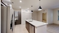 This well-appointed 2-bedroom, 2-bathroom residence offers a thoughtfully designed single-floor layout with modern finishes throughout. The open-concept kitchen and living area serves as the heart of the home, anchored by a large center island with a white quartz countertop, undermount sink, and stylish pendant lighting. Dark wood cabinetry contrasts beautifully with light upper cabinets, a classic tile backsplash, and a full suite of stainless steel appliances, including a French door refrigerator, microwave, and range. Light wood-look flooring flows through the main living areas, while a ceiling fan and French doors leading to an outdoor space add both function and natural light to the living room. Both bedrooms feature plush carpeting, ceiling fans, and windows with blinds that invite natural light. The primary bedroom is generously sized and includes a dedicated closet with built-in wire shelving for organized storage. Each bathroom is finished with dark wood vanities, white quartz countertops, large framed mirrors, and tile-surround walk-in showers with glass enclosures, set on contemporary tile flooring. Two additional closets provide ample storage throughout the residence.