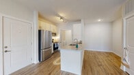 Located at 225 Sandalwood Cir in Brunswick, Georgia, this one-bedroom, one-bathroom residence offers a well-designed single-floor layout with modern finishes throughout. The open-concept living and kitchen area serves as the heart of the home, featuring warm hardwood-style flooring, neutral walls, and a ceiling fan that enhances comfort and airflow. Natural light filters in through a window, brightening the living space.

The kitchen is a standout feature, equipped with stainless steel appliances including a refrigerator, microwave, and range. White shaker-style cabinetry provides ample storage, while a kitchen island with a striking marble-look countertop and an undermount sink adds both functionality and visual appeal. Track lighting overhead ensures the workspace is well-illuminated.

The bedroom offers a comfortable footprint with the same hardwood-style flooring and direct access to a spacious walk-in closet outfitted with wire shelving and hanging rods on multiple walls, providing generous storage capacity.

The bathroom is finished with tile flooring, a marble-look vanity countertop, and a framed glass walk-in shower. A dedicated laundry room with a top-load washer and overhead wire shelving adds everyday convenience to this thoughtfully arranged residence.