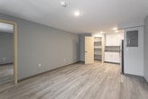 Located at 216 Parkway Drive in Williamsburg, Virginia, this single-floor unit offers a clean, modern interior with a cohesive design throughout. Light hardwood-style flooring spans the entire space, creating a bright and consistent aesthetic that complements the soft blue-gray painted walls and white trim.

The open living area is spacious and airy, benefiting from a large multi-pane window that fills the room with natural light and offers views of surrounding greenery. A wall-mounted HVAC unit provides individual climate control, and a recessed ceiling light adds to the well-lit atmosphere.

The kitchen is well-appointed with white shaker-style cabinetry, granite-look countertops, and a full suite of stainless steel appliances including a refrigerator, range, and microwave. A walk-in pantry or storage closet is conveniently accessible directly from the kitchen, providing ample additional storage space.

The bathroom is neatly finished with a white vanity cabinet topped with a dark granite-pattern countertop and undermount sink, accented by brushed gold hardware. A large mirror, a combined shower/tub unit, and light flooring complete the space with a polished, updated feel.

Overall, this unit presents a fresh and functional living environment with modern finishes, practical storage, and natural light, ideally situated in the historic Williamsburg area.