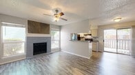 Located at 5341 Gawain Dr in San Antonio, TX, this single-floor 2-bedroom, 2-bathroom unit offers a practical and comfortable layout. Wood-look luxury vinyl plank flooring runs throughout, providing a cohesive and easy-to-maintain foundation across all rooms. The combined kitchen and living area serves as the heart of the home, where a galley-style kitchen features white cabinetry, grey countertops, a mosaic tile backsplash, and black appliances including a range and refrigerator. A peninsula counter connects the kitchen to the living space, which is highlighted by a brick-surround fireplace with a distinctive herringbone wood accent panel above the mantle. Natural light filters in through multiple windows. The spacious primary bedroom includes dual sliding-door closets and a ceiling fan, while the second bedroom also offers a sliding-door closet and a window with natural light. Both bathrooms are appointed with tiled shower-tub combinations, wood-look flooring, and overhead cabinetry for storage. Neutral grey walls and clean white trim throughout give the space a fresh, move-in ready appearance.