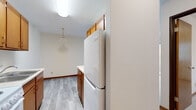 This single-floor unit offers a practical and functional layout with a clean, neutral aesthetic throughout. The living area is bright and open, featuring light gray hardwood-style flooring, warm wood baseboard trim, and a sliding glass door that leads to a private balcony overlooking lush greenery, filling the space with natural light and outdoor views.

The kitchen is efficiently designed with warm-toned wood cabinetry, white appliances including an electric range and full-size refrigerator, a single-basin sink, and ample counter space. A pendant light fixture adds a subtle decorative touch above the kitchen's dining area transition. The kitchen flows naturally into the main living space, creating an open and connected feel.

The bedroom features plush neutral carpet, a built-in sliding-door closet with shelving and hanging space, and a baseboard heating unit, offering a comfortable and practical retreat.

The bathroom is straightforward and functional, featuring a white vanity with storage, an integrated sink, a mirrored medicine cabinet, and a bathtub. Crisp white finishes throughout keep the space feeling clean and well-maintained. Baseboard heating is present throughout the unit, ensuring year-round comfort.