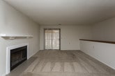 This single-floor unit offers a practical and comfortable layout with clearly defined living spaces. The spacious living room serves as the centerpiece of the home, featuring plush wall-to-wall carpeting, a wood-burning fireplace with a clean white mantel, and a sliding glass door that allows natural light to fill the room. A ceiling fan is positioned nearby, providing additional ventilation and airflow. The open layout connects the living room directly to the kitchen, creating a cohesive and functional flow.

The galley-style kitchen is equipped with oak-toned cabinetry, laminate countertops, and black appliances, including a full-size refrigerator. Wood-look vinyl flooring runs throughout the kitchen, adding a warm contrast to the neutral walls. A dedicated laundry area houses a full-size top-loading washer and dryer, adding everyday convenience.

The bedrooms feature neutral carpet, textured ceilings, and windows that bring in natural light. The bathroom is outfitted with wood-look vinyl flooring, a full soaking tub with tiled surround, a toilet, and a vanity with granite-style countertops. White walls and clean finishes maintain a consistent, understated aesthetic throughout the unit.