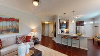 This single-floor residence offers a thoughtfully designed layout that balances comfort and functionality throughout its connected living spaces. Crown molding and rich hardwood-style flooring establish a consistent, polished aesthetic across the main living areas.

The living room is bright and welcoming, benefiting from multiple windows that allow natural light to fill the space. It connects seamlessly to both the kitchen and dining area, creating an open, cohesive flow. The kitchen is well-equipped with dark espresso cabinetry, granite-style countertops, a full suite of stainless steel appliances including a refrigerator, electric range, and built-in microwave, and a breakfast bar with pendant lighting overhead. An adjacent dining nook features a chandelier and large windows dressed with decorative curtains, creating an intimate yet airy setting.

Both bedrooms are carpeted and comfortably scaled, each featuring ceiling fans and windows that bring in natural light. The bathroom includes an extended dual-sink vanity with granite-style countertops, dark cabinetry, hardwood-style flooring, and ample mirror space, offering both practicality and a refined finish throughout.