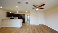 This single-story unit features a cohesive, open-concept design unified by warm wood-look vinyl flooring throughout the main living areas. The living room is generously proportioned, illuminated by recessed lighting and a ceiling fan, and benefits from natural light admitted through a set of French doors that open to the exterior. A front entry door provides a secondary access point.

The kitchen is well-appointed with dark espresso cabinetry offering ample upper and lower storage, light-toned countertops, and a full suite of black appliances including a refrigerator, electric range, built-in microwave, and dishwasher. A peninsula with an extended countertop connects the kitchen to the living area, creating an efficient and sociable layout. Pendant lighting accents the peninsula from above.

Bedroom spaces continue the wood-look flooring and neutral wall palette, each equipped with a ceiling fan and window with blinds for natural light and privacy. The bathroom features light tile flooring, a tub-shower combination with tiled surround, and a separate closet. The clean, neutral palette throughout the unit provides a versatile and move-in-ready environment.